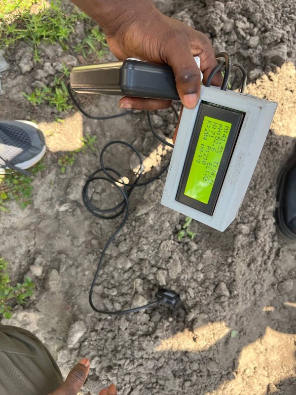 A hand holds the SoilPulse reader above dry soil while the wired probe sits in the ground